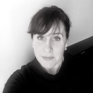 Black and white headshot of Jean smiling softly. Her hair is pulled back and she is wearing a black blouse.